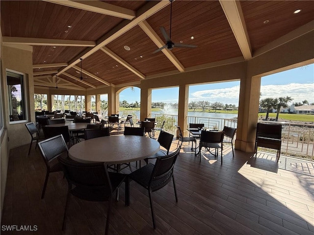 dining room with dark hardwood / wood-style floors, lofted ceiling with beams, ceiling fan, and a water view