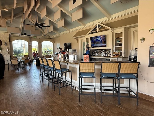 bar with dark wood-style flooring, a ceiling fan, beam ceiling, and a bar