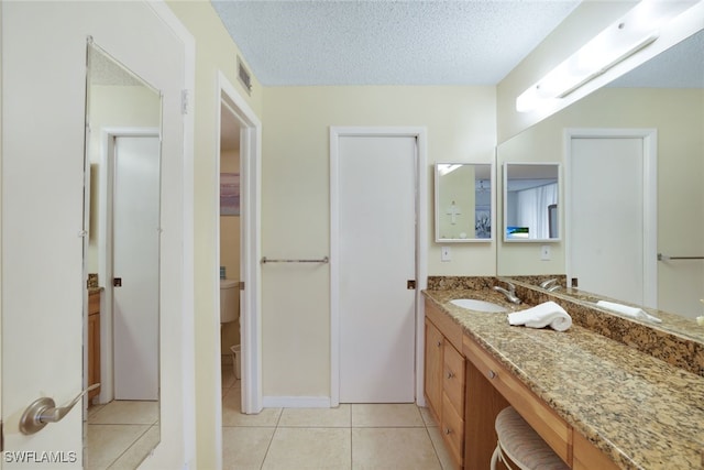 bathroom with a textured ceiling, toilet, tile patterned flooring, and vanity