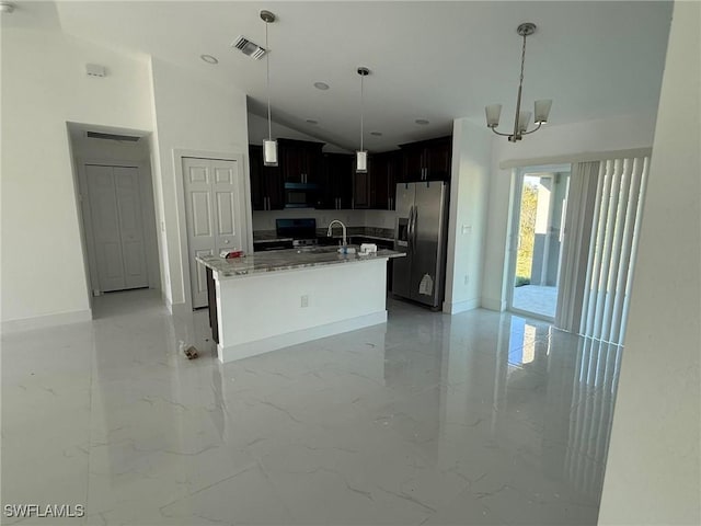 kitchen with stainless steel fridge, light stone counters, a center island with sink, an inviting chandelier, and lofted ceiling