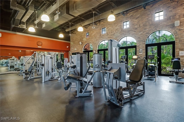 exercise room featuring a high ceiling, brick wall, and french doors