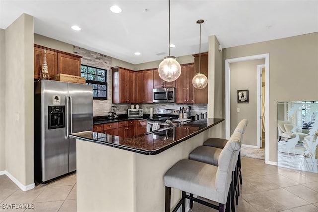 kitchen featuring kitchen peninsula, appliances with stainless steel finishes, decorative light fixtures, light tile patterned flooring, and a breakfast bar