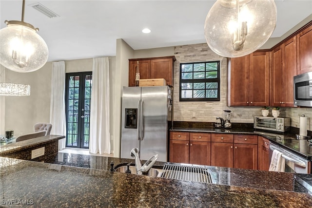 kitchen featuring french doors, dark stone counters, hanging light fixtures, and stainless steel appliances