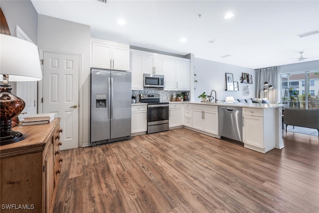 kitchen featuring hardwood / wood-style floors, white cabinets, stainless steel appliances, decorative backsplash, and kitchen peninsula