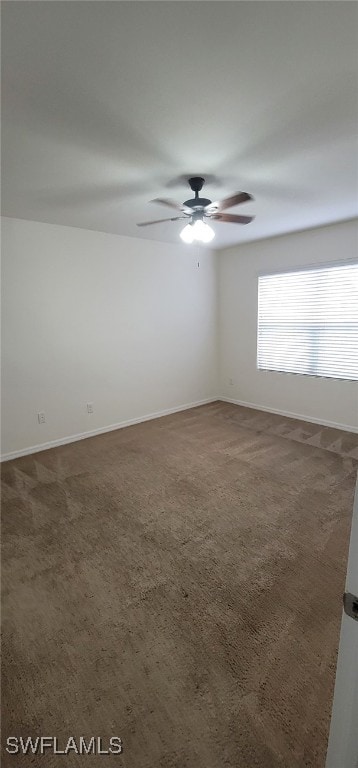 spare room featuring dark colored carpet and ceiling fan