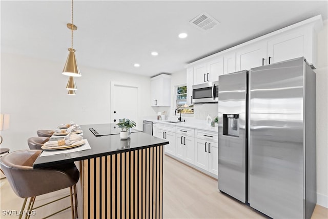 kitchen featuring white cabinets, sink, appliances with stainless steel finishes, decorative light fixtures, and light hardwood / wood-style floors