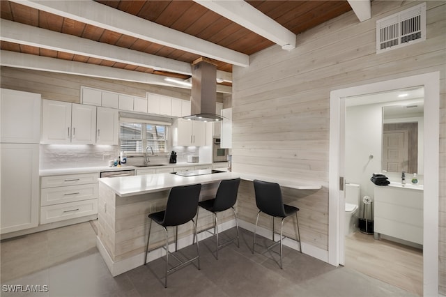 kitchen with white cabinetry, island range hood, a breakfast bar, and wood walls