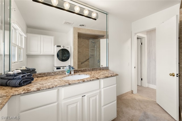 bathroom featuring tiled shower, stacked washer / drying machine, tile patterned flooring, and vanity