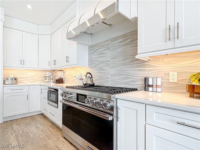 kitchen with backsplash, high end stainless steel range, light hardwood / wood-style flooring, light stone counters, and white cabinetry