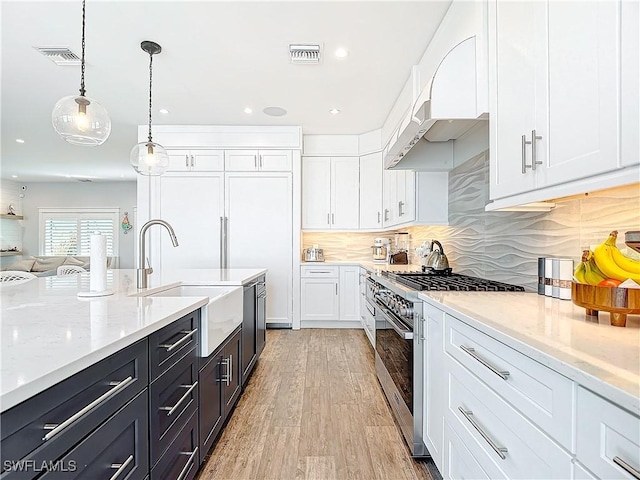 kitchen featuring white cabinetry, sink, pendant lighting, stainless steel stove, and light wood-type flooring