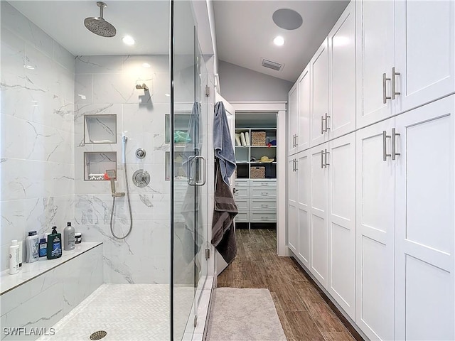 bathroom with wood-type flooring, vaulted ceiling, and a shower with shower door