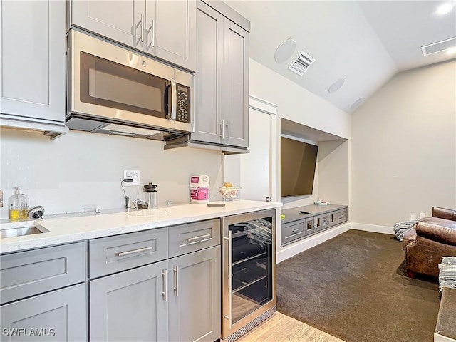 kitchen with gray cabinetry, sink, vaulted ceiling, light stone counters, and beverage cooler