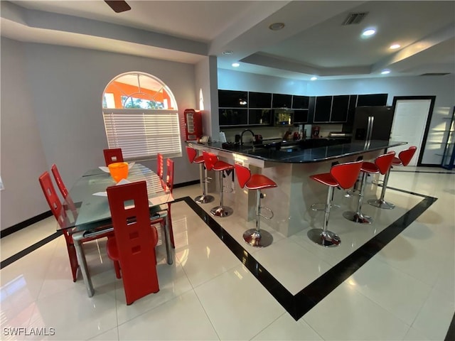 kitchen featuring a kitchen breakfast bar, light tile patterned flooring, a raised ceiling, and black refrigerator with ice dispenser