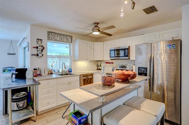 kitchen with backsplash, white cabinetry, appliances with stainless steel finishes, ceiling fan, and sink