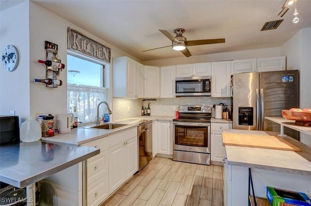 kitchen with stainless steel appliances, decorative backsplash, white cabinets, ceiling fan, and sink