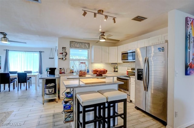 kitchen featuring ceiling fan, stainless steel appliances, white cabinetry, and a kitchen bar