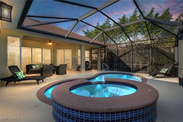 pool at dusk featuring a lanai, a patio, outdoor lounge area, ceiling fan, and an in ground hot tub