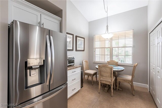 kitchen featuring vaulted ceiling, light tile patterned floors, white cabinets, hanging light fixtures, and stainless steel fridge