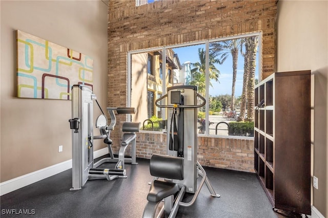 exercise room featuring brick wall and a high ceiling