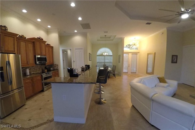 kitchen with tasteful backsplash, stainless steel appliances, ceiling fan, a center island with sink, and a breakfast bar area