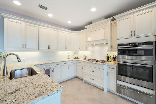 kitchen featuring sink, stainless steel appliances, light stone counters, backsplash, and custom exhaust hood