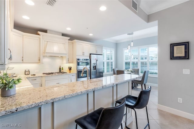 kitchen with a kitchen bar, appliances with stainless steel finishes, premium range hood, light tile patterned floors, and decorative light fixtures