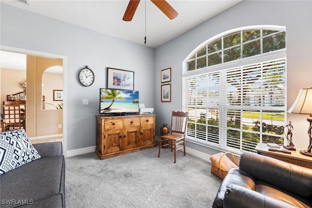 living area with arched walkways, light colored carpet, ceiling fan, and baseboards