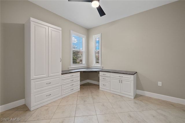 unfurnished office with built in desk, ceiling fan, and light tile patterned flooring