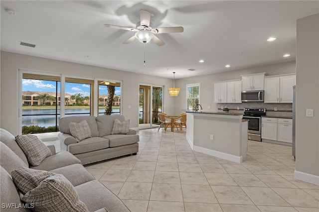 living room featuring ceiling fan, light tile patterned flooring, a healthy amount of sunlight, and a water view