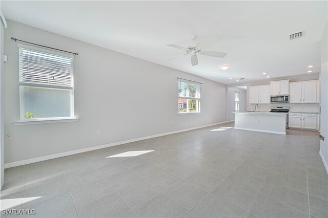 unfurnished living room with ceiling fan, light tile patterned floors, and sink