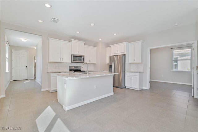 kitchen featuring stainless steel appliances, light tile patterned floors, tasteful backsplash, an island with sink, and white cabinets