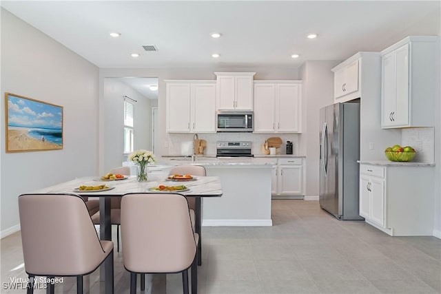 kitchen featuring appliances with stainless steel finishes, light stone counters, a breakfast bar, white cabinetry, and an island with sink