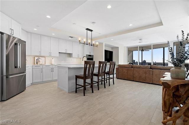 kitchen with a breakfast bar area, stainless steel appliances, an island with sink, hanging light fixtures, and white cabinetry