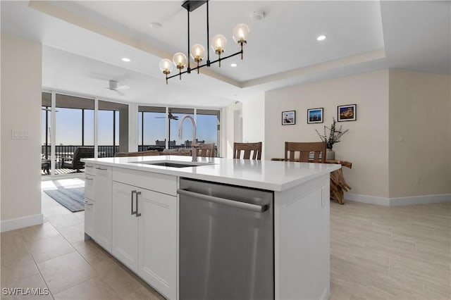 kitchen featuring floor to ceiling windows, stainless steel dishwasher, an island with sink, a raised ceiling, and white cabinetry