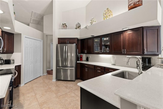 kitchen featuring sink, a towering ceiling, kitchen peninsula, dark brown cabinetry, and appliances with stainless steel finishes