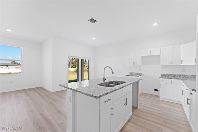 kitchen featuring light stone countertops, white cabinetry, a kitchen island with sink, and sink