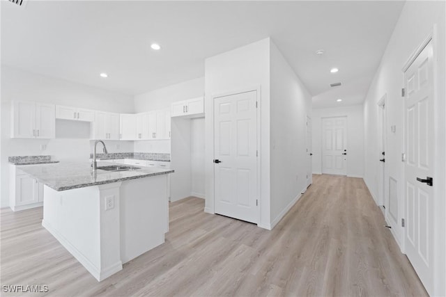 kitchen with sink, light stone counters, light hardwood / wood-style floors, a kitchen island with sink, and white cabinets