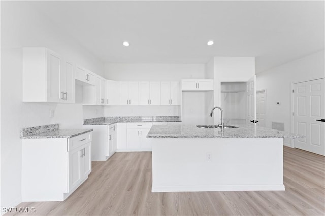 kitchen featuring a kitchen island with sink, sink, white cabinets, and light stone countertops