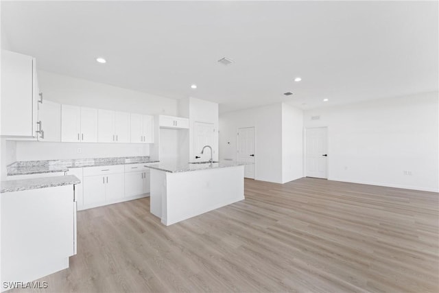 kitchen with light hardwood / wood-style floors, light stone counters, white cabinetry, and a kitchen island with sink