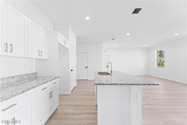 kitchen featuring white cabinetry, sink, light stone counters, light hardwood / wood-style flooring, and a kitchen island with sink