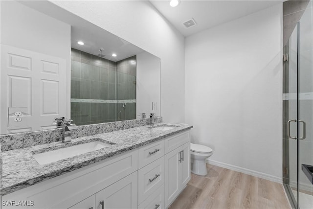 bathroom featuring wood-type flooring, vanity, a shower with shower door, and toilet