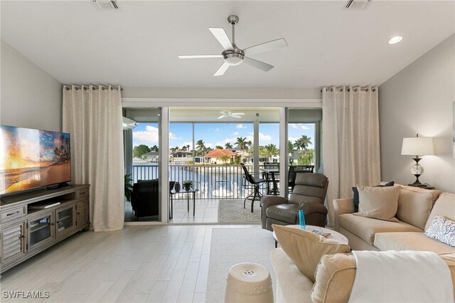 living room featuring ceiling fan, a water view, and light wood-type flooring