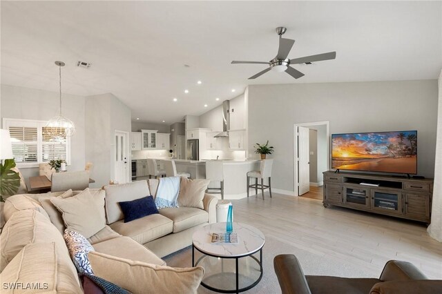 living room with vaulted ceiling, ceiling fan with notable chandelier, and light hardwood / wood-style flooring