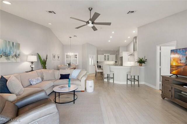 living room featuring lofted ceiling, ceiling fan with notable chandelier, and light hardwood / wood-style flooring