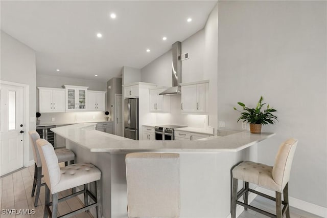 kitchen featuring a kitchen bar, kitchen peninsula, appliances with stainless steel finishes, wall chimney range hood, and white cabinets