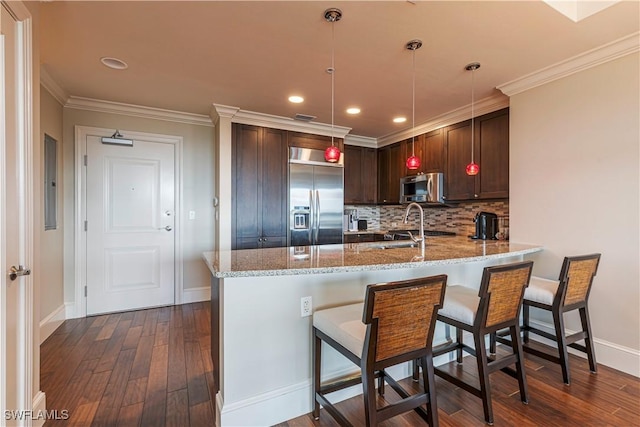 kitchen with appliances with stainless steel finishes, light stone counters, dark wood-type flooring, ornamental molding, and a peninsula