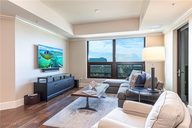 living room with wood finished floors, ornamental molding, a raised ceiling, and baseboards