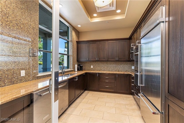 kitchen featuring light stone counters, backsplash, appliances with stainless steel finishes, a sink, and dark brown cabinets