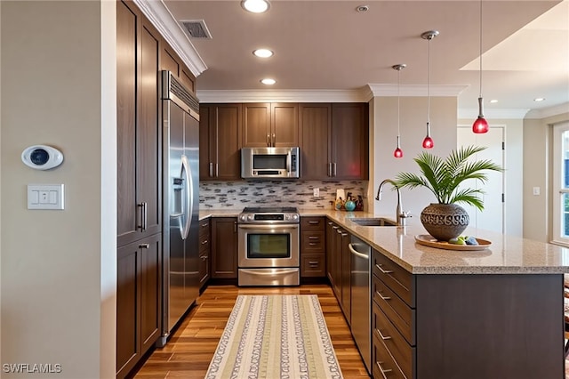 kitchen with a sink, appliances with stainless steel finishes, a peninsula, light wood finished floors, and backsplash