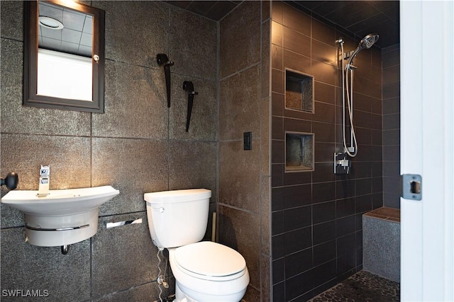 bathroom with a tile shower, toilet, and tile walls